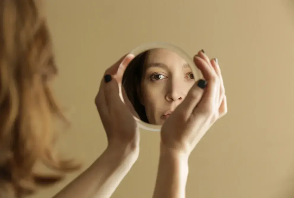 Frau schaut in Spiegel und reflektiert sich selbst